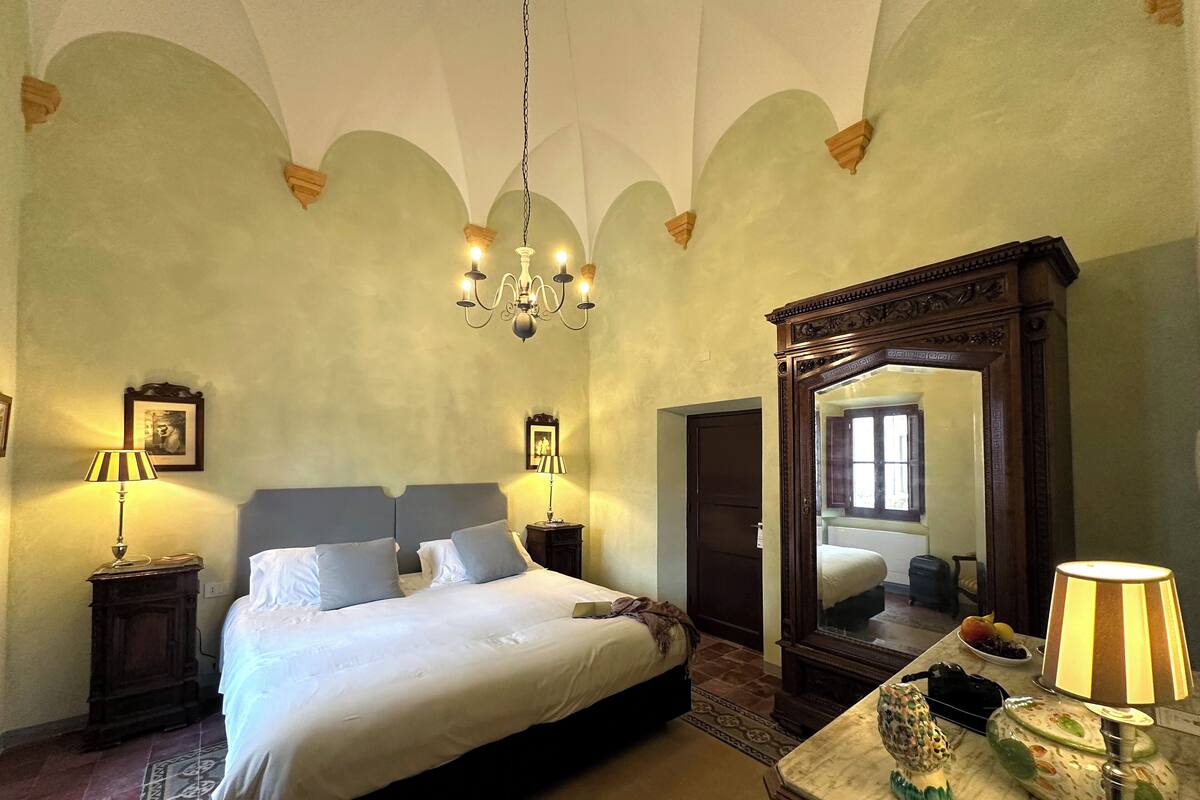 A bedroom with a large bed, a chandelier, a mirror, and a dresser with decorative items.