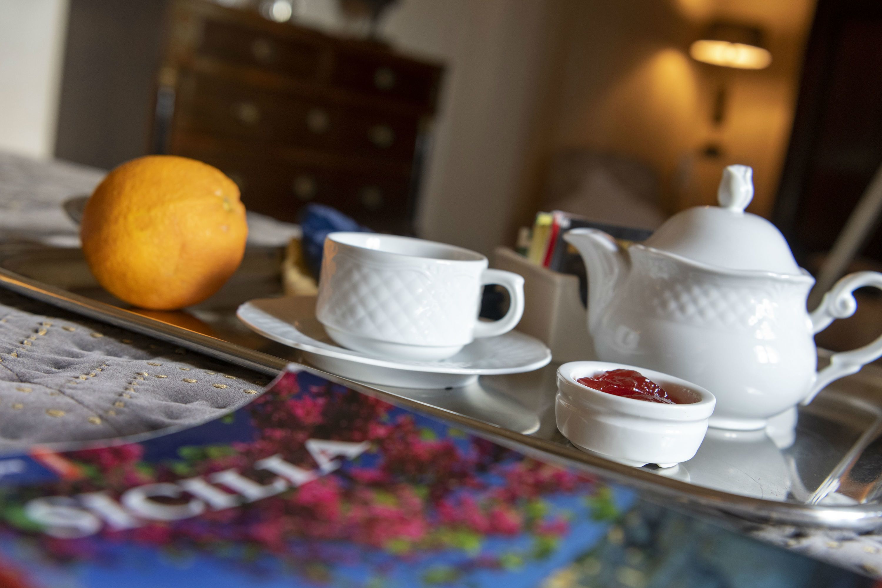 Una bandeja con tetera, tazas y un recipiente pequeño de mermelada, colocada sobre una mesa con una revista.