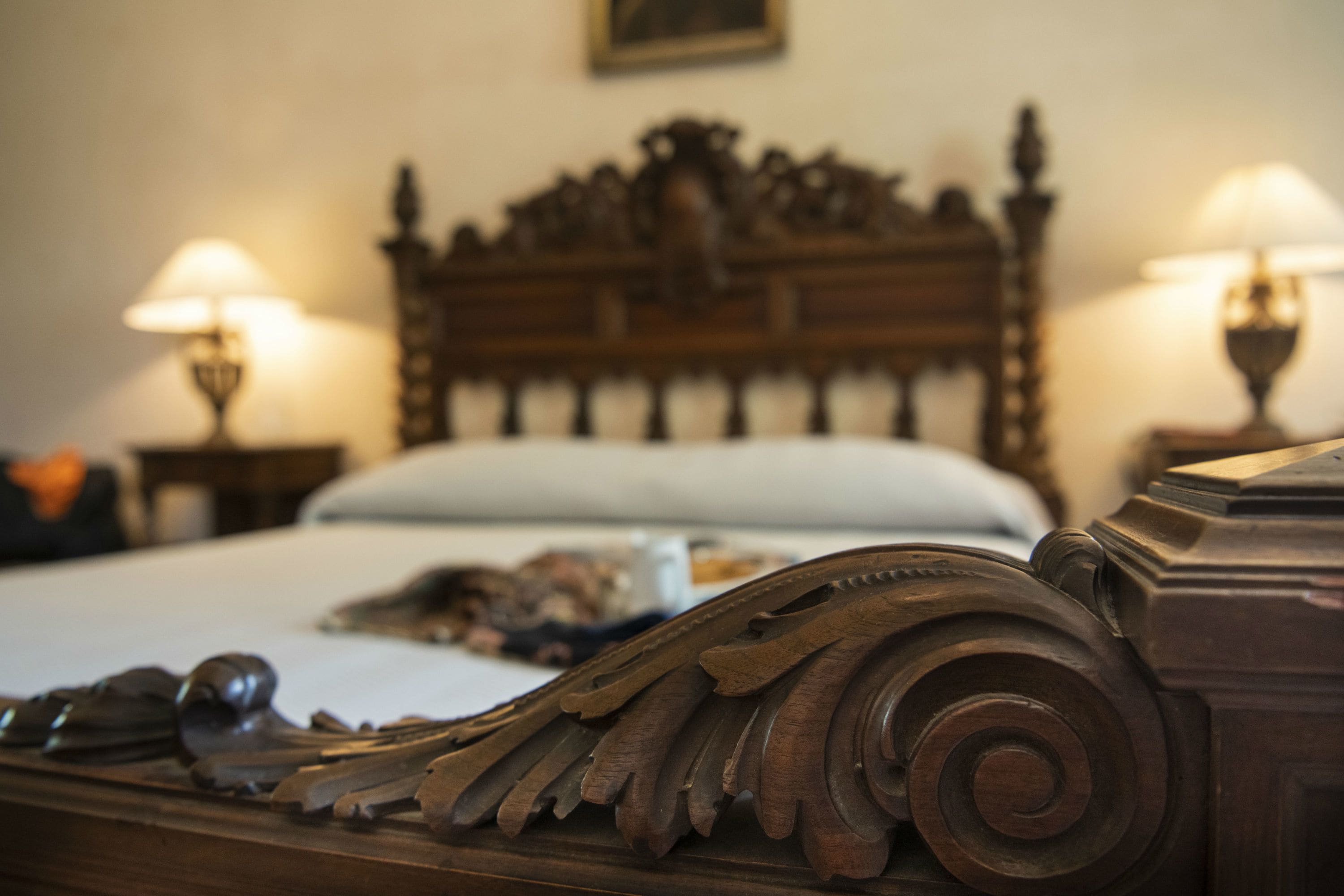 A wooden bed with intricate carvings, two bedside lamps, and a white pillow.