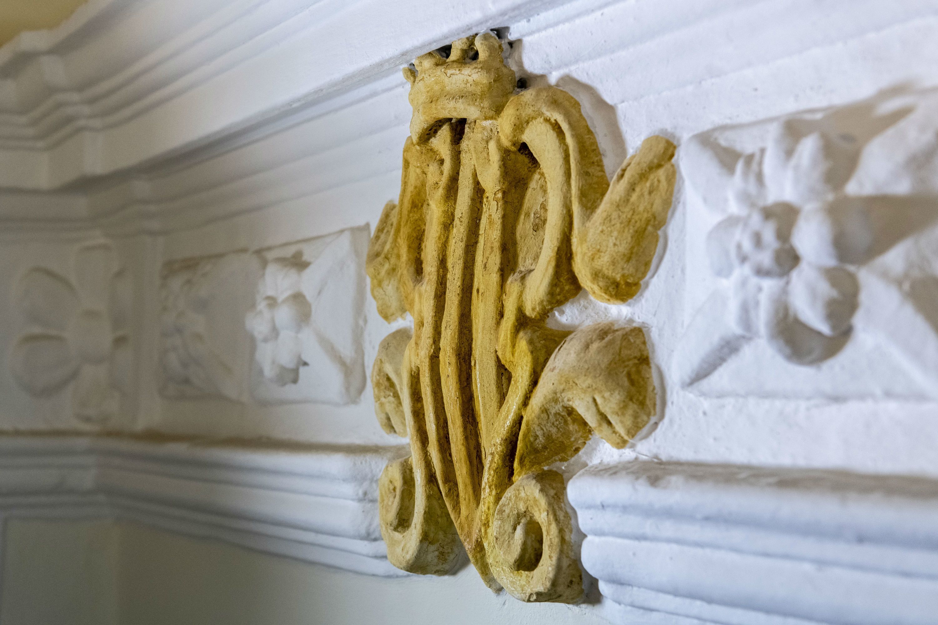 Une sculpture architecturale détaillée orne un mur blanc, représentant un motif floral et une figure classique.