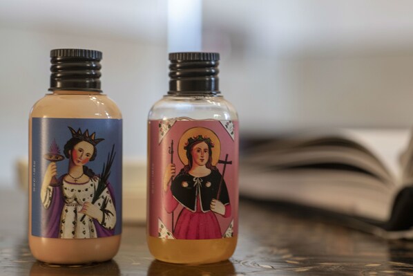 Dos botellas con etiquetas de temática religiosa sobre una superficie reflectante.