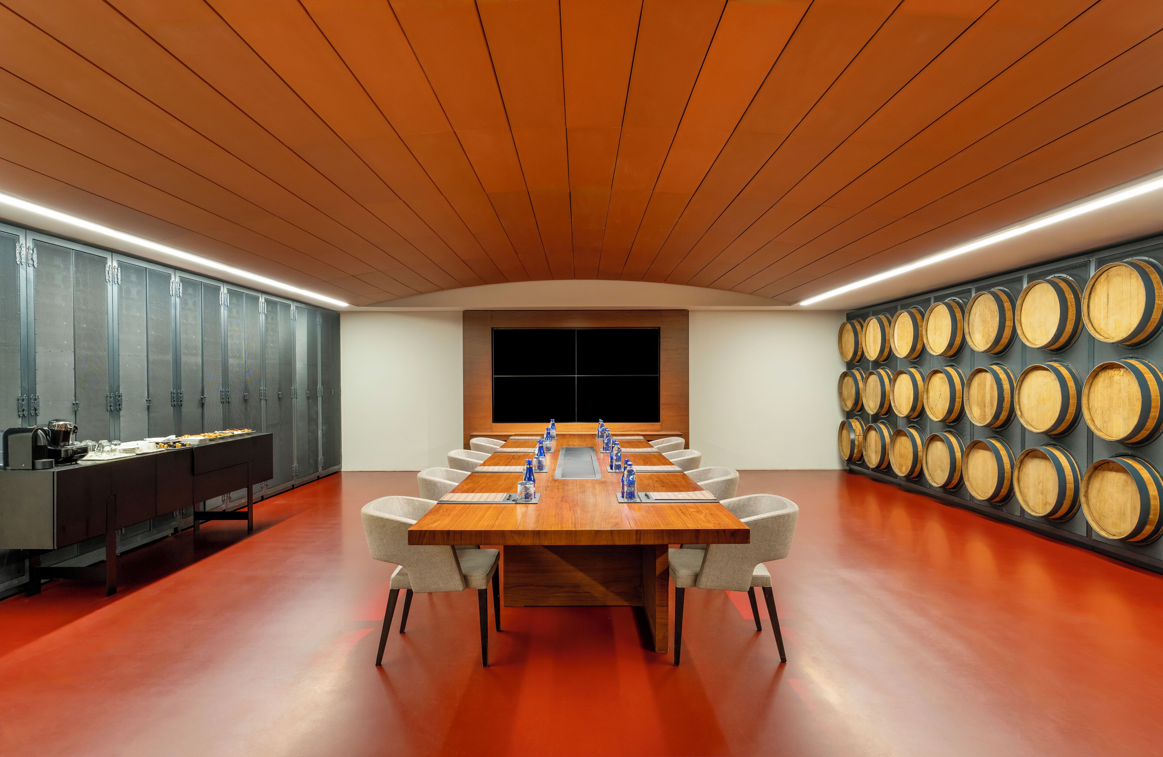Una sala de conferencias con una larga mesa, sillas, una mesa de buffet y una pared de barriles de madera.