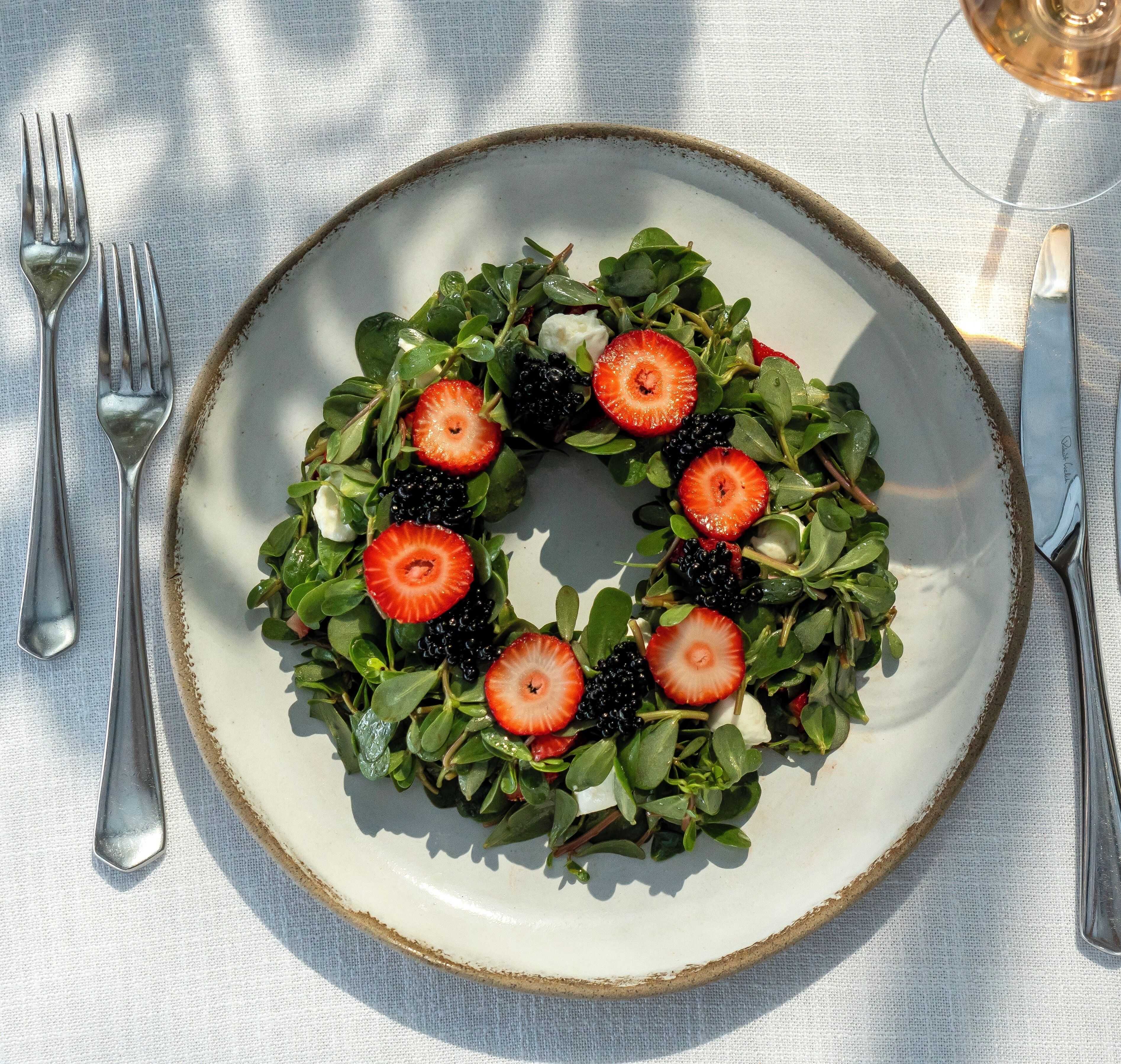 A plate with a salad of greens and strawberries.