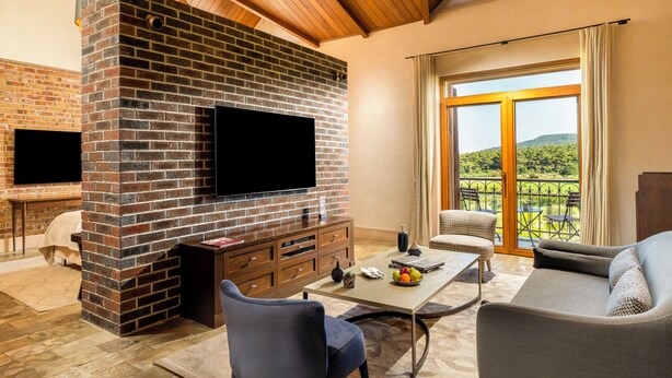 Una sala de estar con chimenea de ladrillo, televisor de pantalla plana, mesa de comedor con sillas y vista a un balcón con mobiliario exterior.
