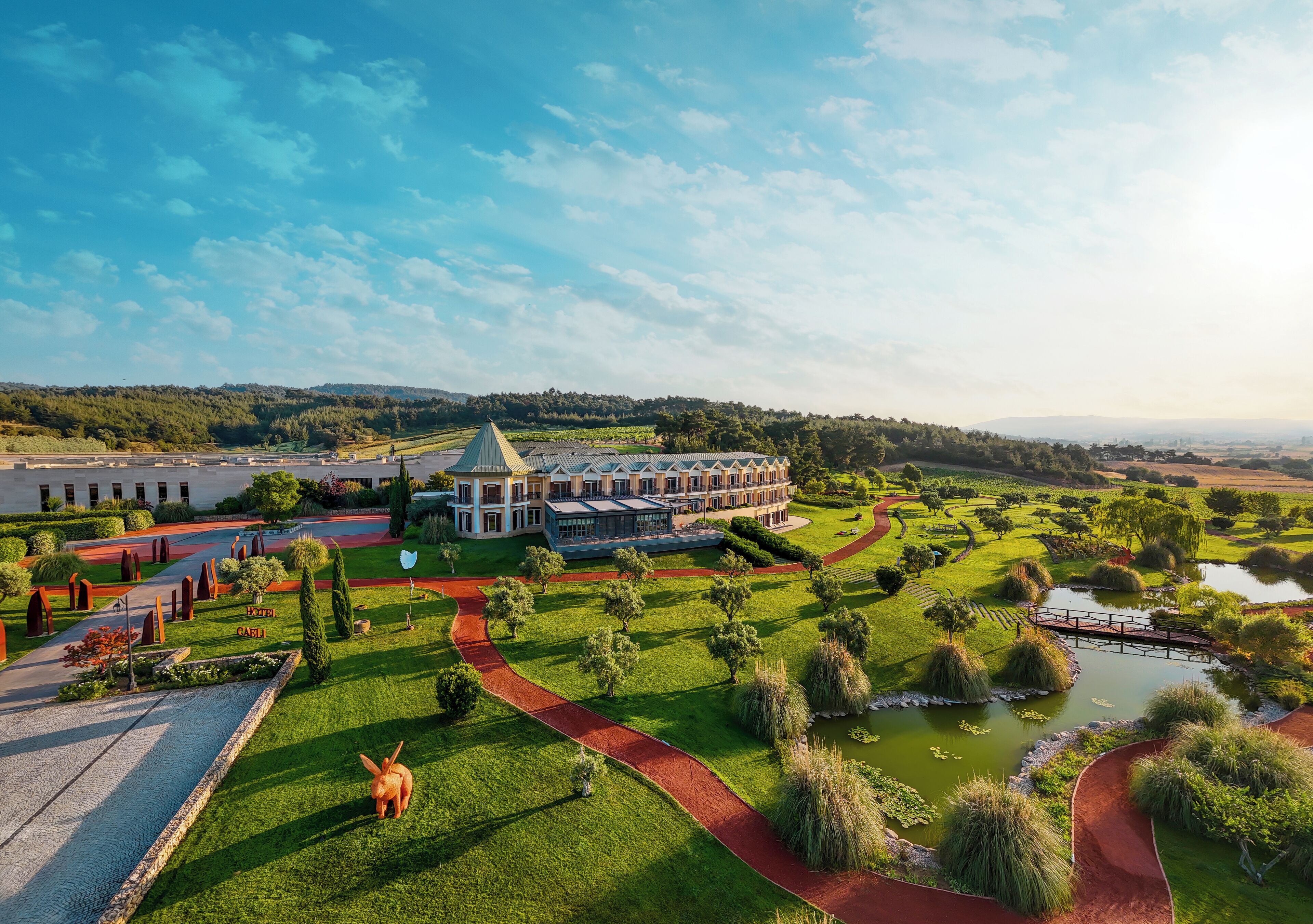 A large, modern hotel with a central courtyard, surrounded by lush greenery and a small pond.