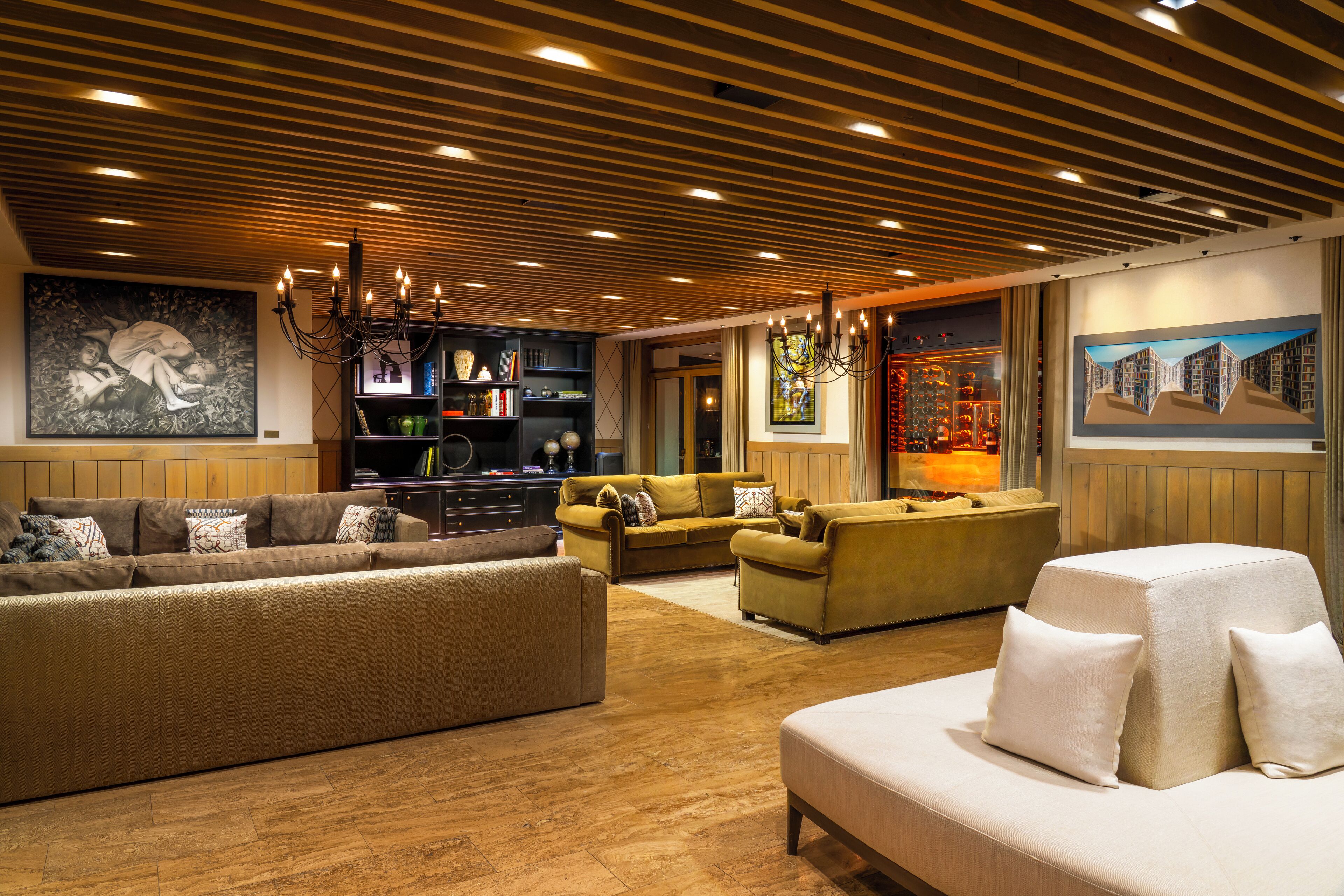 A spacious living room with a wooden ceiling, a large sofa, a smaller sofa, and a white bench. There are bookshelves and artwork on the walls.