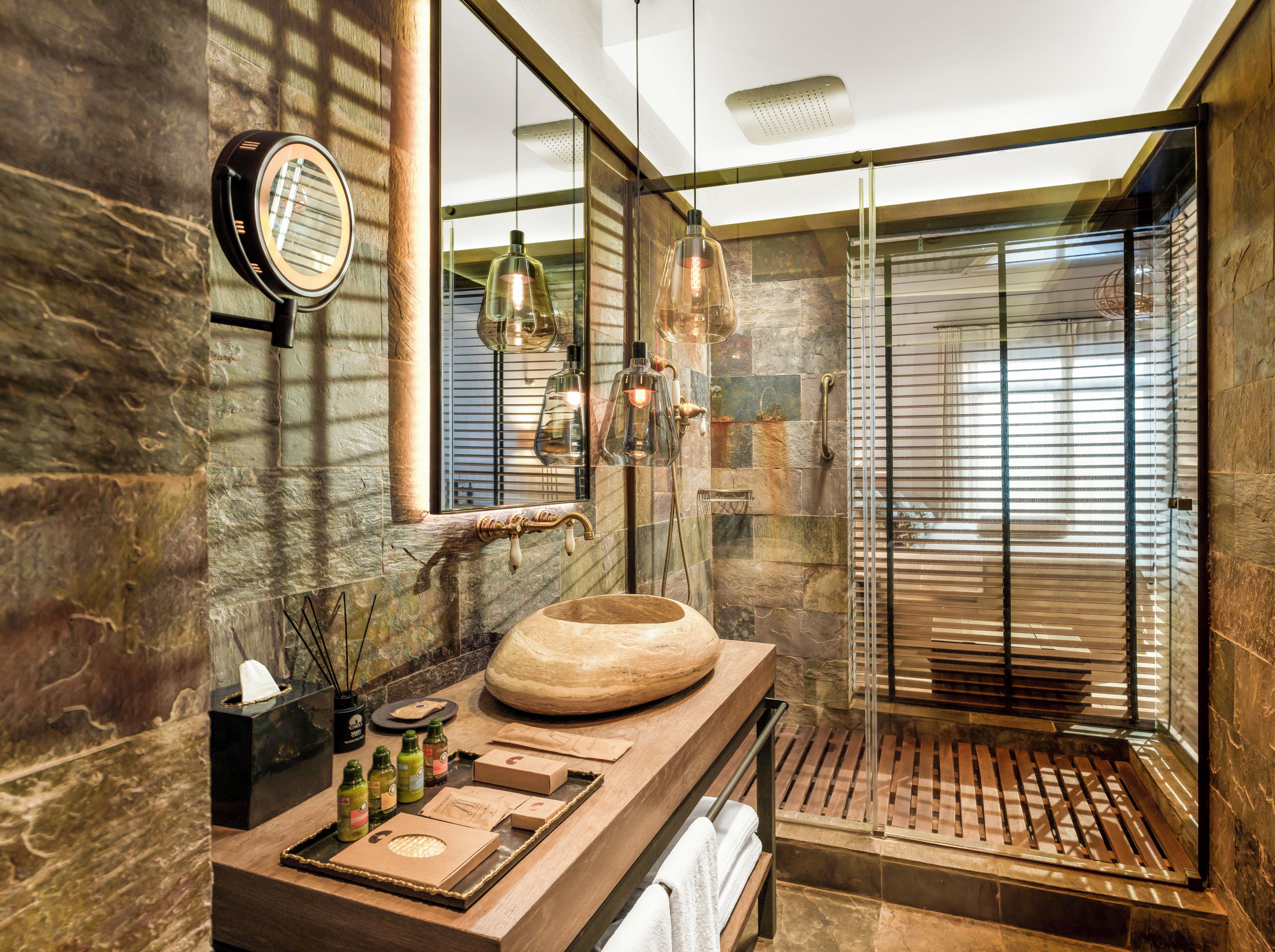 Un baño moderno con un lavamanos de piedra, un espejo grande y una zona de ducha con mampara de vidrio.