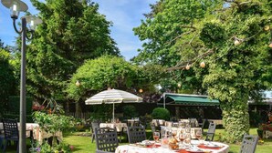 Un área de comedor al aire libre con mesas dispuestas para una comida, rodeada de abundante follaje y árboles.