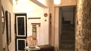 Um interior acolhedor com um banco de madeira, uma mesa pequena e um tapete estampado. Uma cadeira está posicionada perto do banco, e uma escada é visível ao fundo.