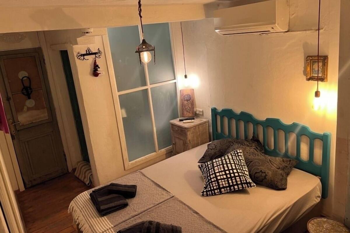 Une chambre à coucher comprenant un lit, une table de chevet, un climatiseur fixé au mur et une fenêtre à vitrage dépoli.