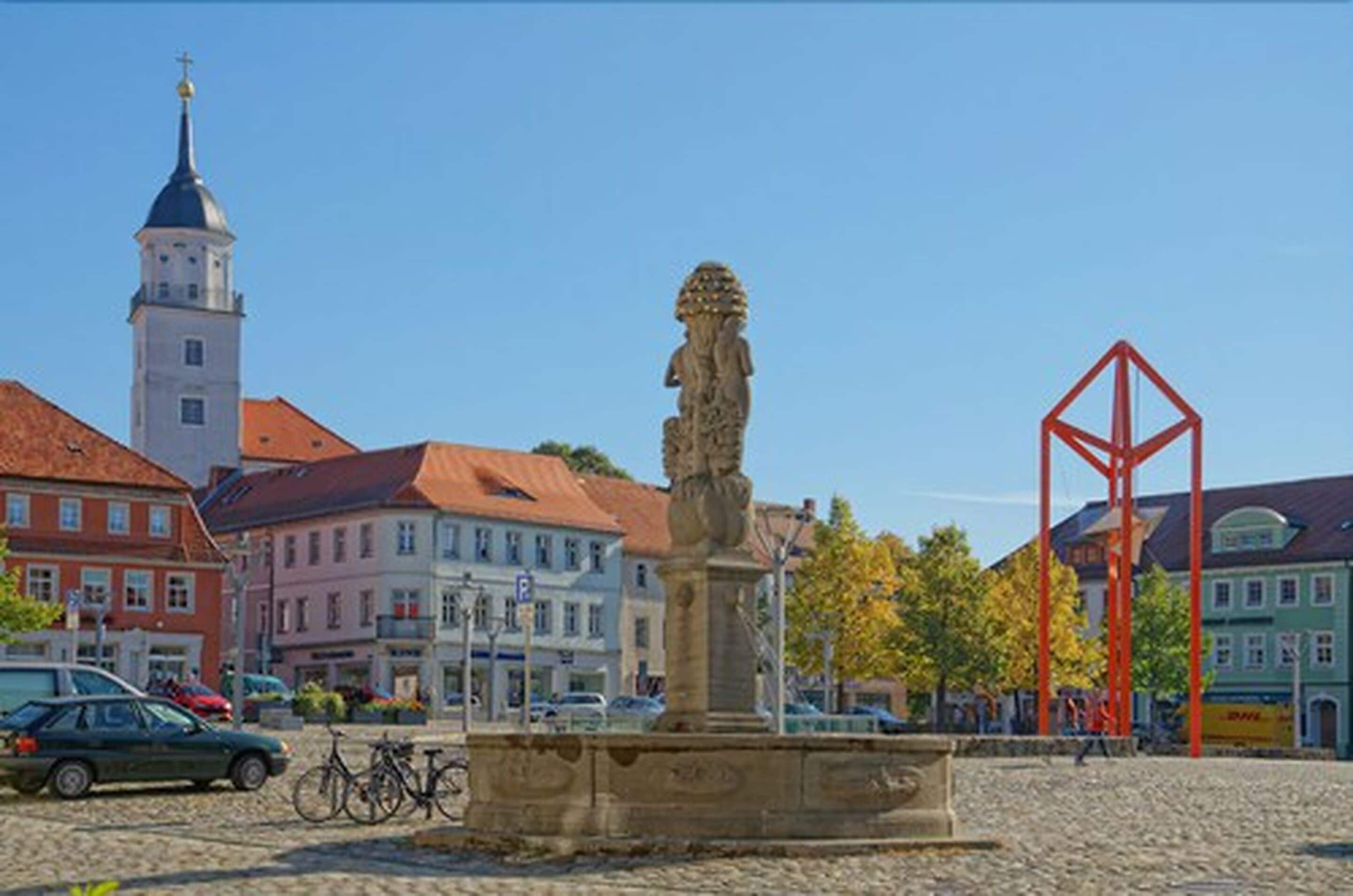 A historic square with a statue, a church tower, and traditional buildings.
