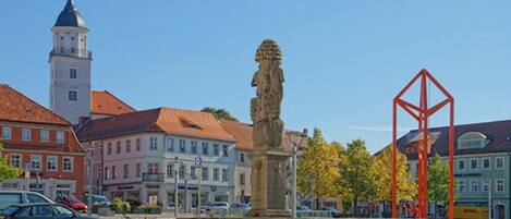 Una plaza histórica con una estatua, una torre de iglesia y edificios tradicionales.