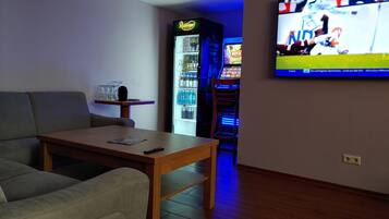 A living room with a sofa, a wooden coffee table, a television mounted on the wall, and a slot machine in the background.