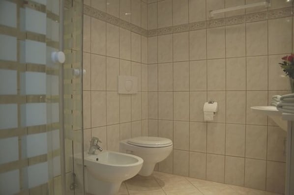 Un baño con inodoro, bidé y cabina de ducha de vidrio.