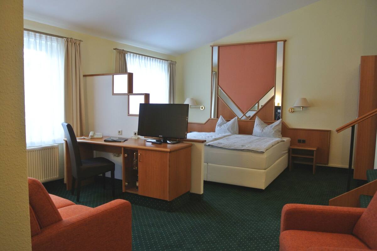 A hotel room with a bed, desk, chair, television, and a small table.