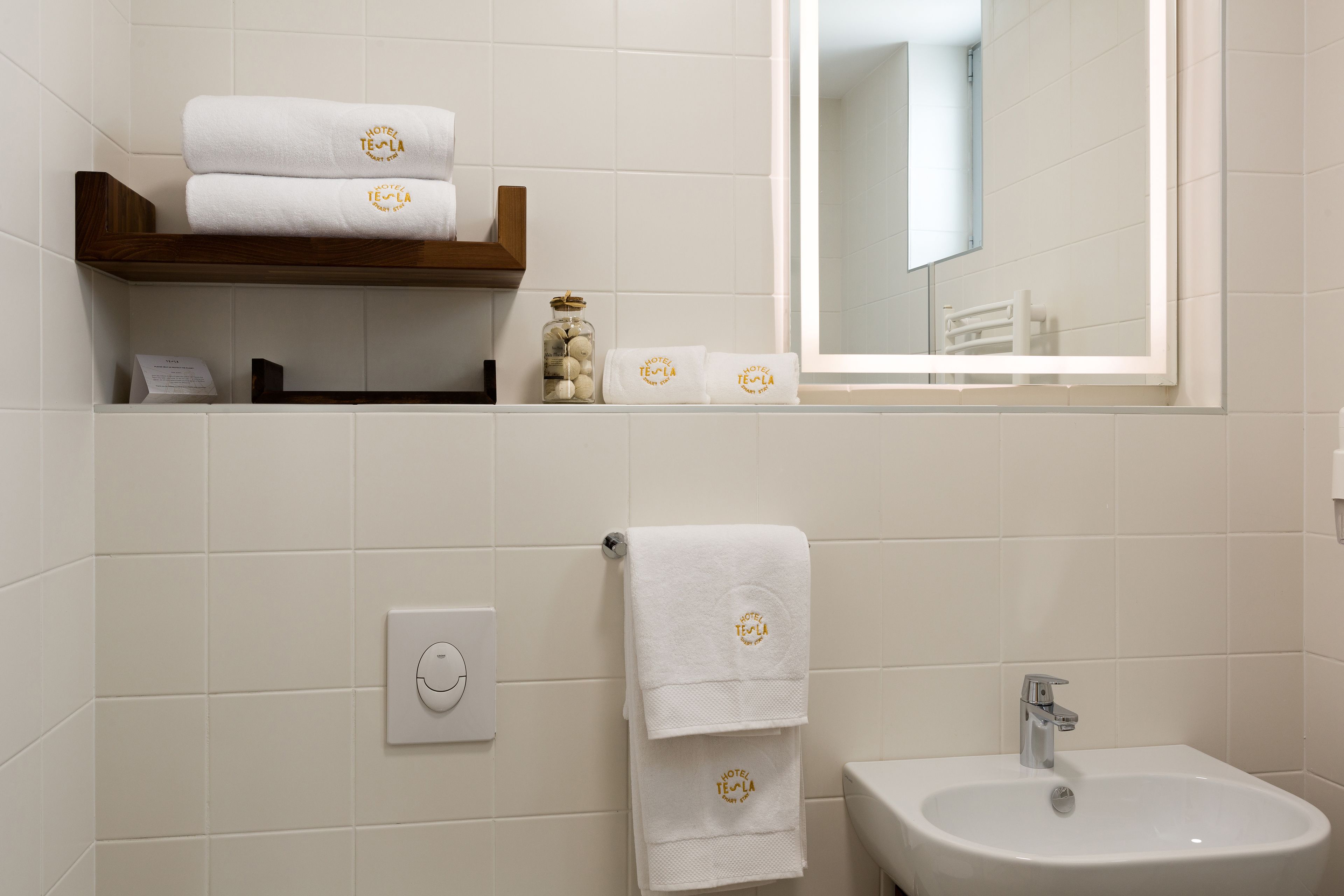 A bathroom with white tiles, a sink, a mirror, and a towel rack with towels.