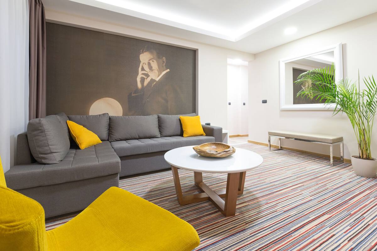 A modern living room with a grey sofa, yellow cushions, a round coffee table, and a large abstract painting on the wall.