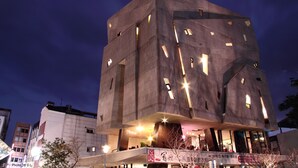 A modern building with a unique angular design, featuring multiple illuminated windows and a prominent entrance area. - Smoking Rock Resort (Jiaoxi)