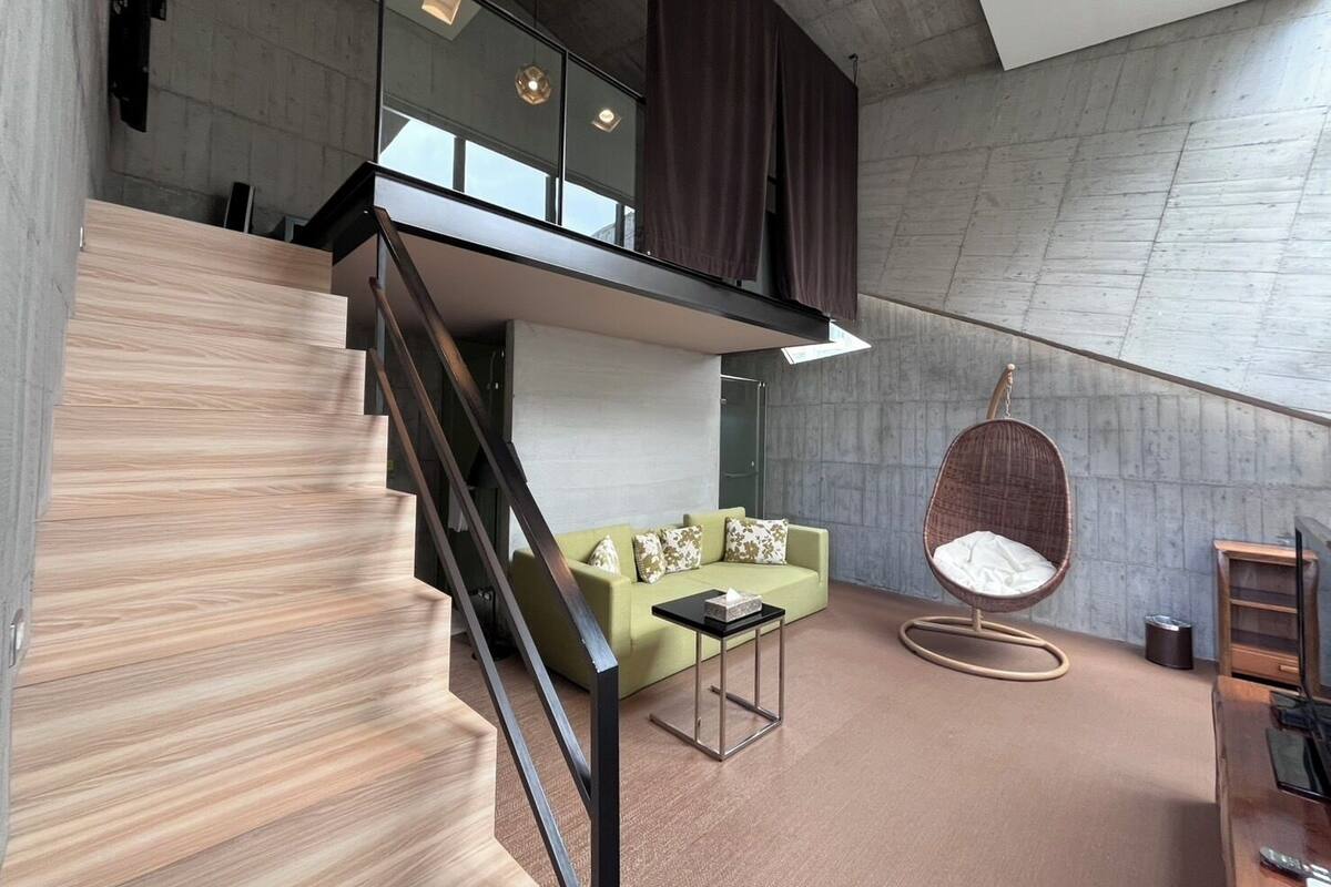 A modern interior with a staircase, a green sofa, a hanging chair, and a minimalist design.
