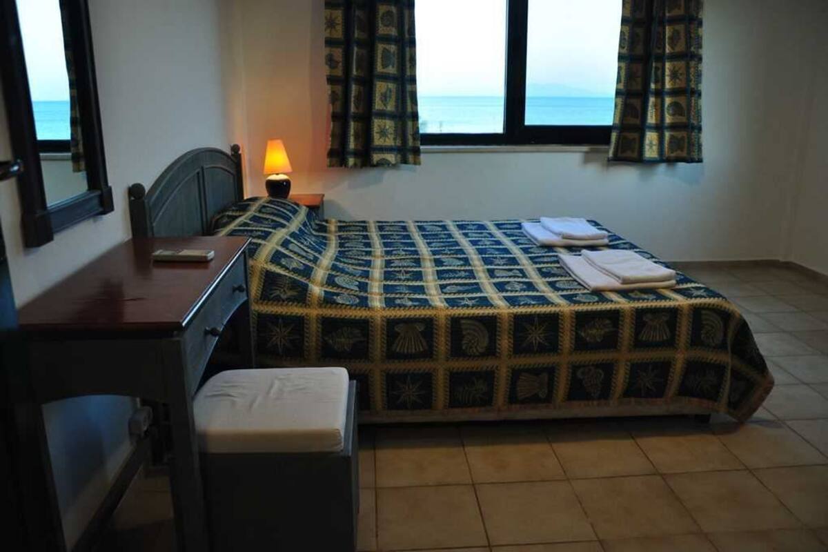 A bedroom with a bed, a desk, a chair, a lamp, and a window with curtains.
