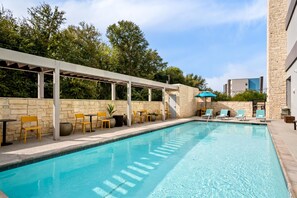 Une piscine entourée de murs de pierre et de verdure, avec des chaises longues et des tables à proximité.