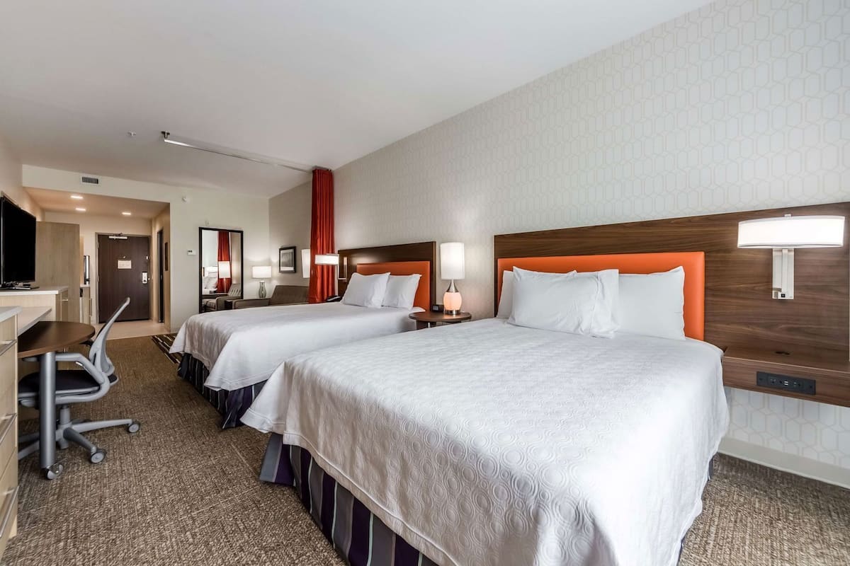 Quarto de hotel com duas camas, uma escrivaninha, uma cadeira e uma televisão.