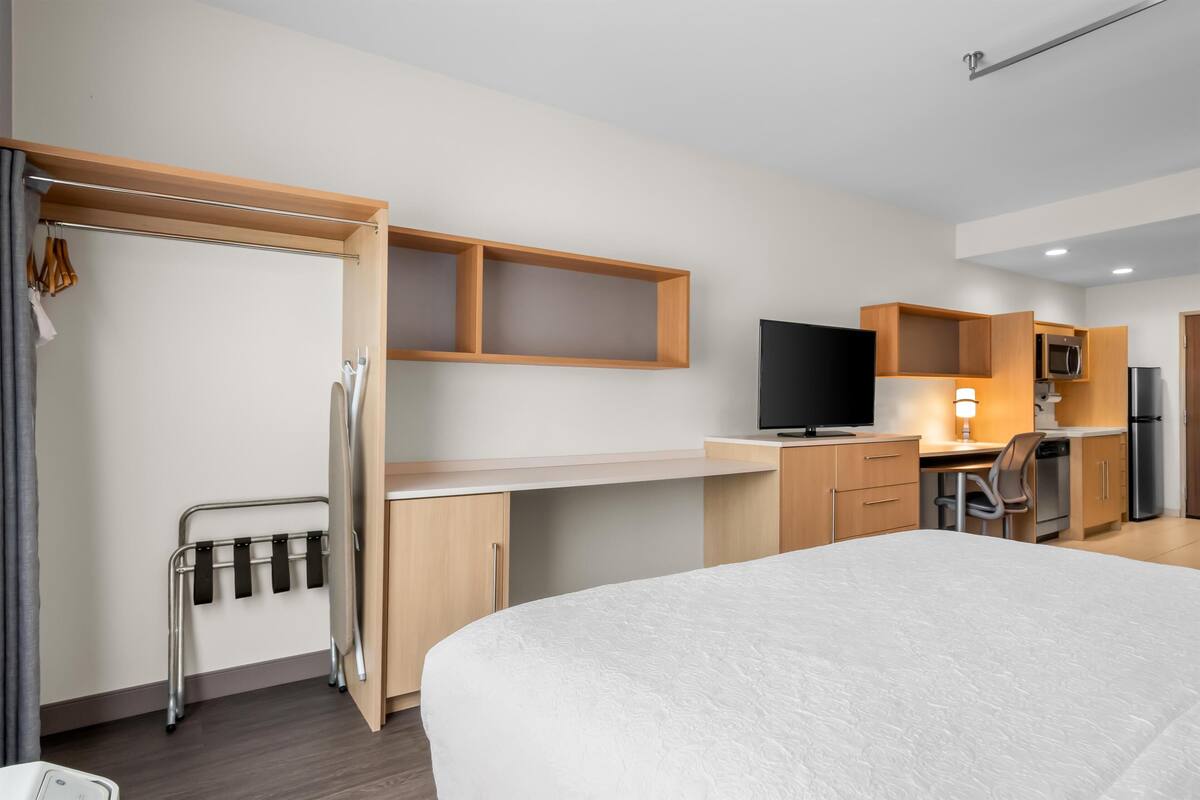 Habitación de hotel con cama, escritorio con televisor, kitchenette y armario.