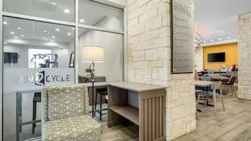 A modern hotel lobby with a reception desk, seating area, and a visible gym sign.
