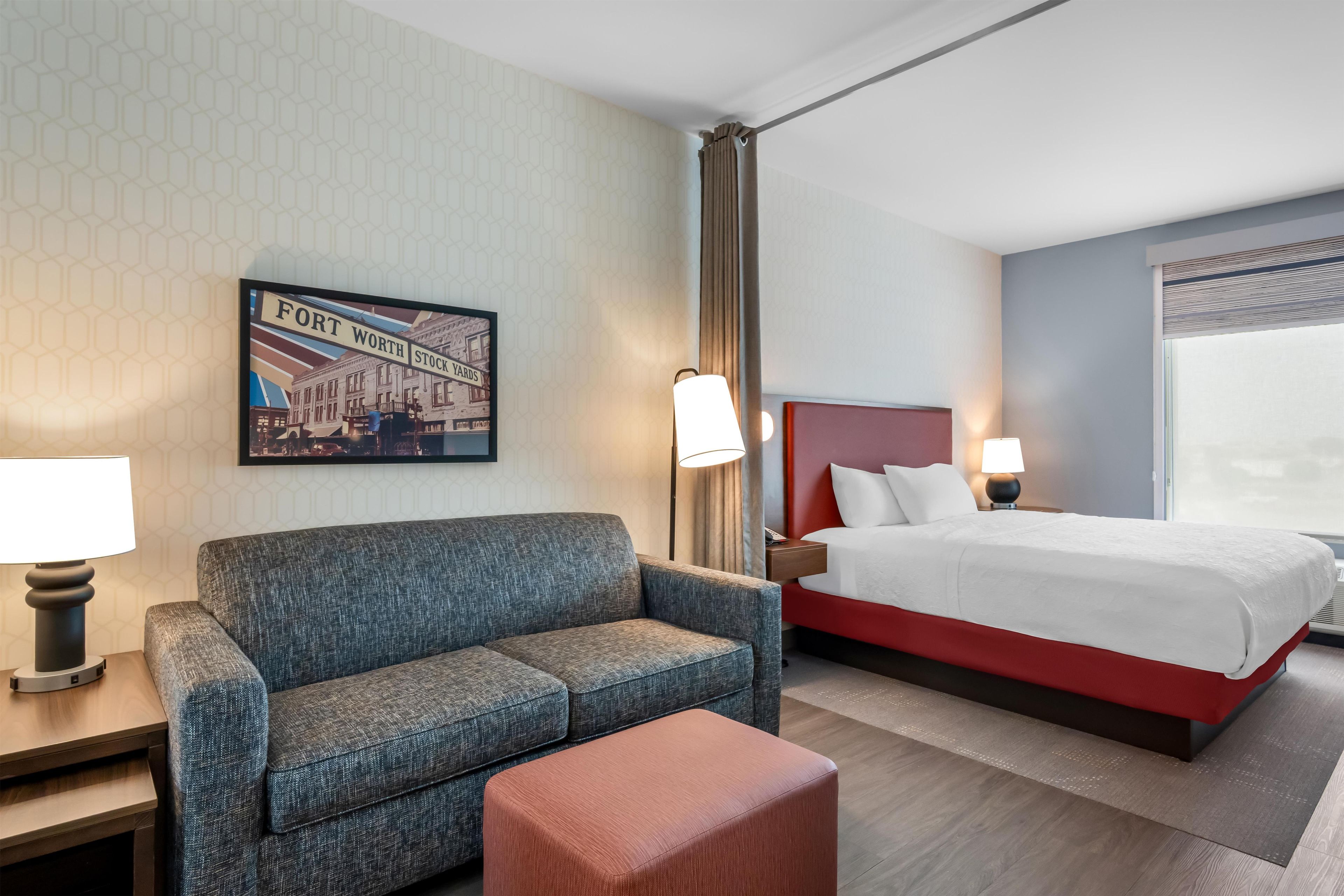 Habitación de hotel con cama, sofá, una mesita, lámpara y un cuadro de Fort Worth Stockyards.
