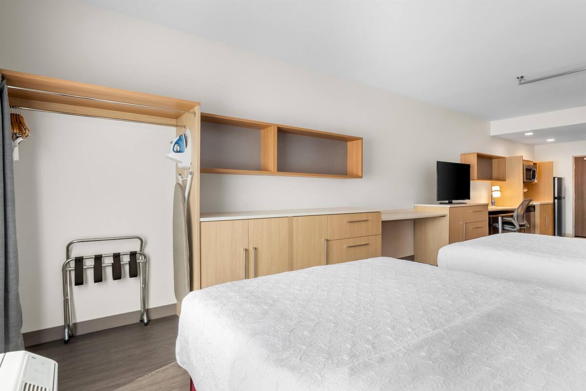 Habitación de hotel con dos camas, un escritorio, televisor y kitchenette.
