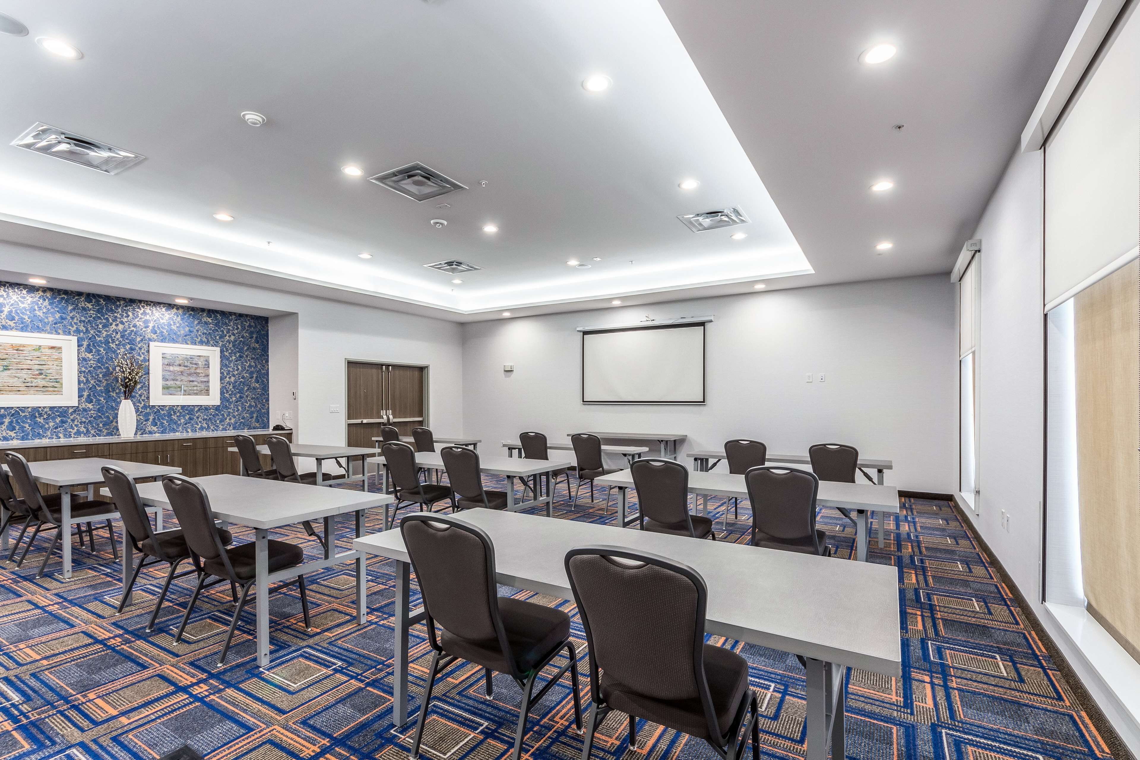 A conference room with tables and chairs, a projector screen, and a patterned carpet.