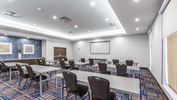 A conference room with tables and chairs, a projector screen, and a patterned carpet.