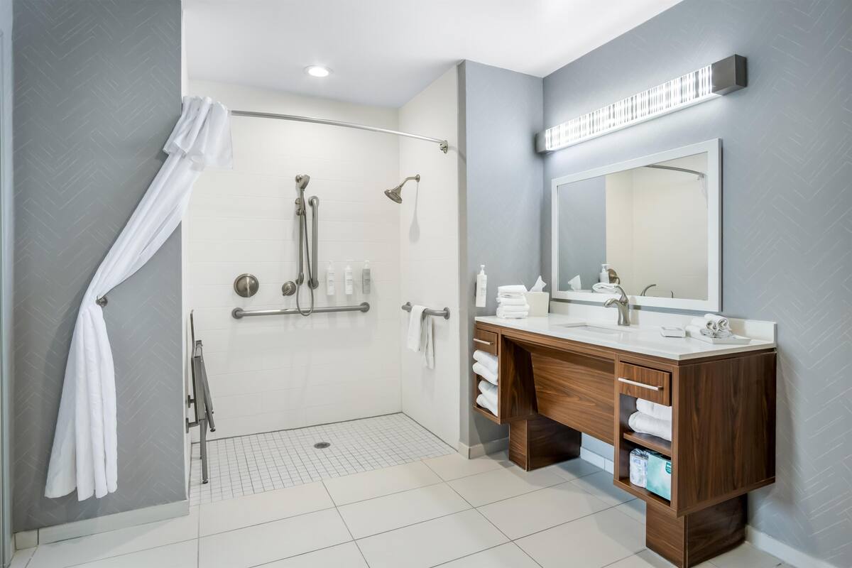 Un baño moderno con ducha, tocador con espejo y perchero para toallas.