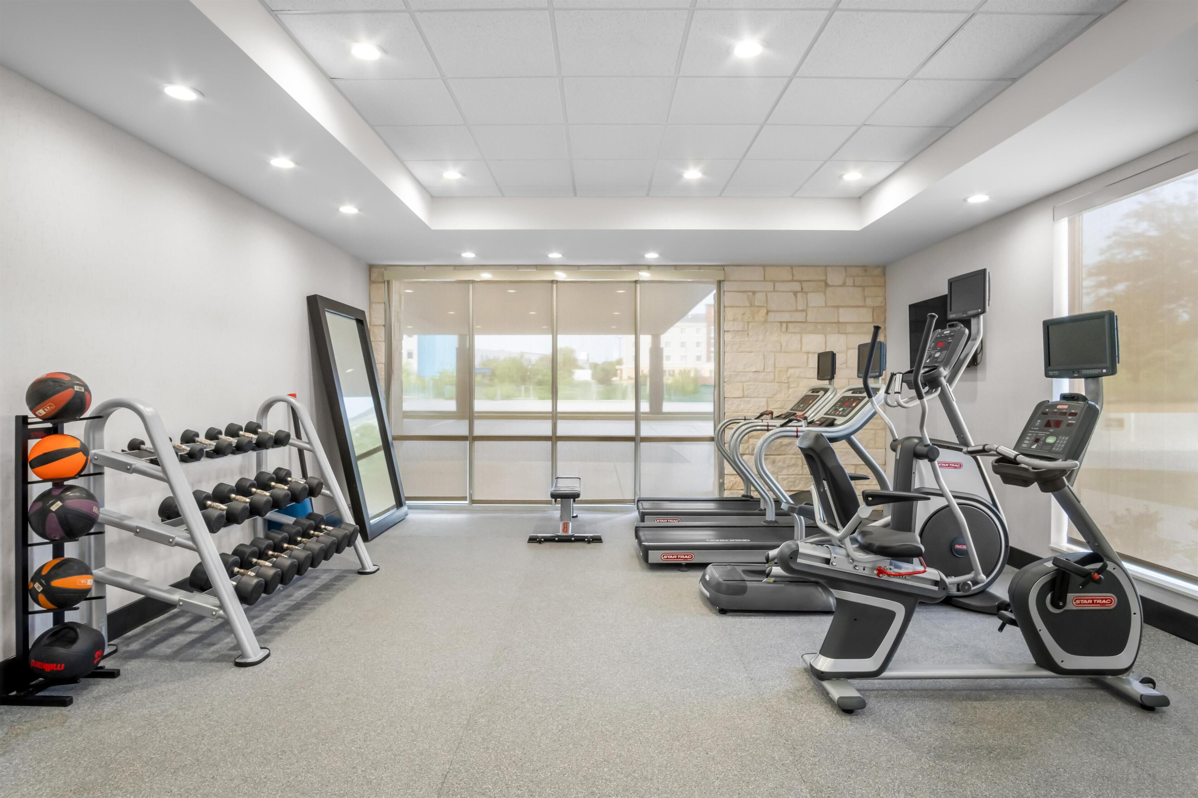 A gym with treadmills, elliptical machines, a mirror, and a rack of dumbbells.