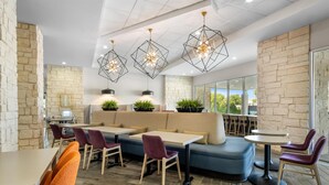 A modern restaurant interior with stone walls, wooden flooring, and a mix of seating options including tables, chairs, and a sofa. - Home2 Suites by Hilton Fort Worth Northlake (Roanoke)