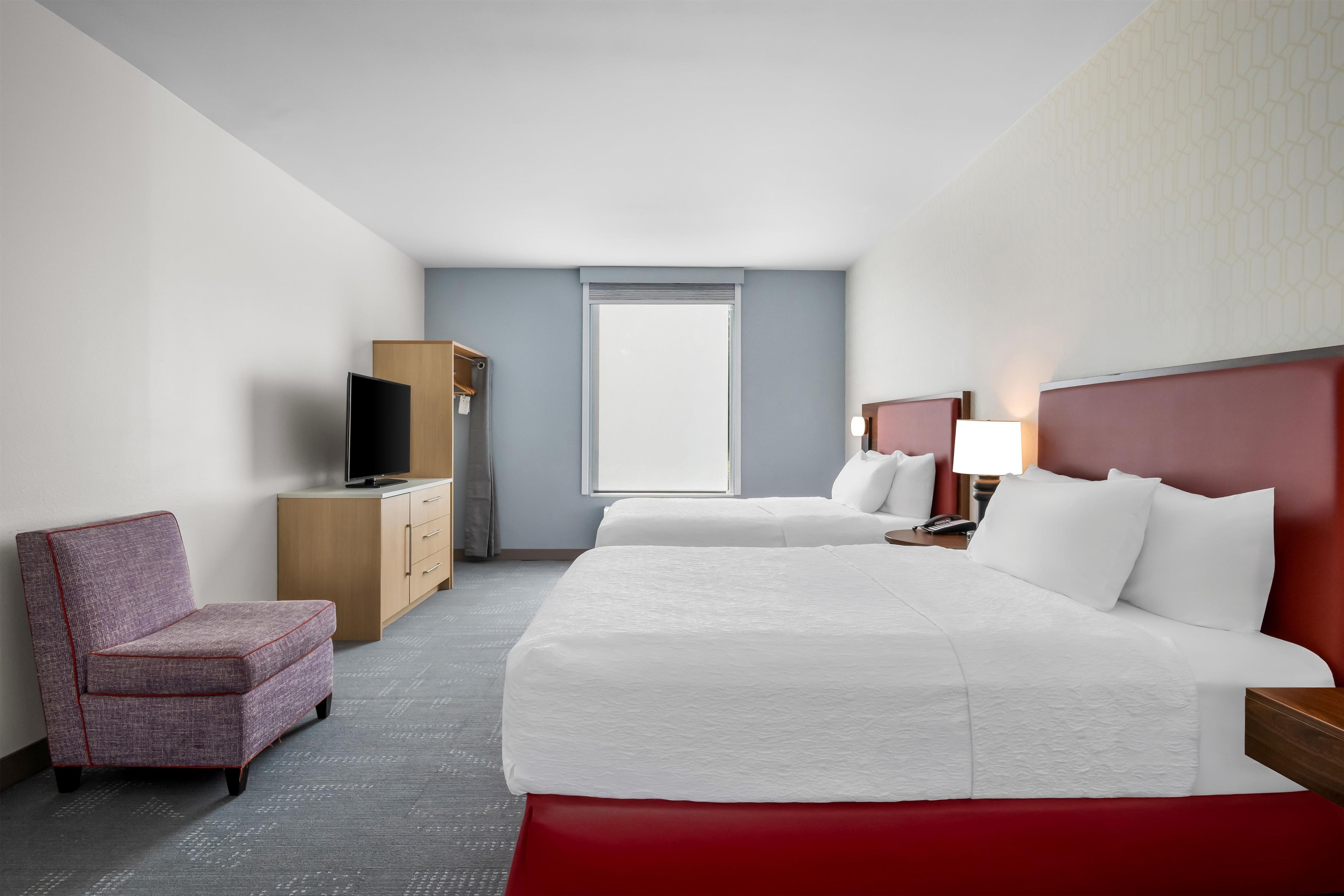 Una habitación de hotel con cama, una silla, televisión, escritorio y ventana.
