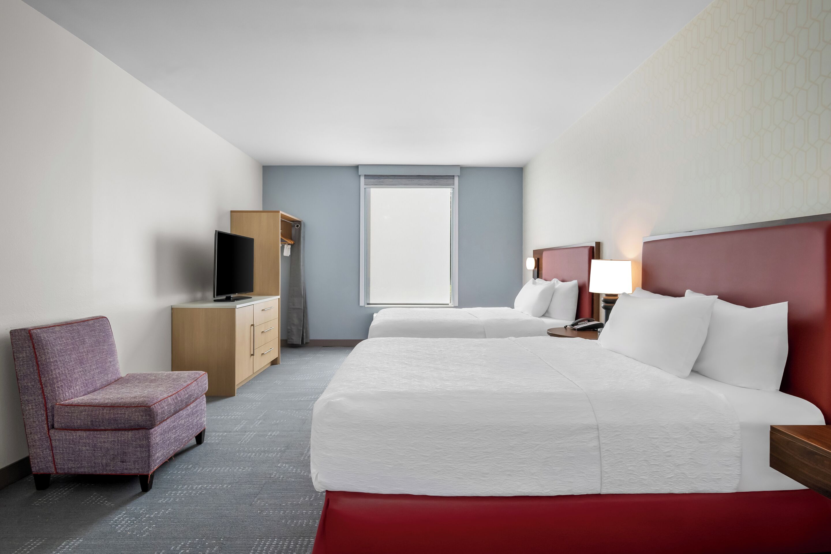 Quarto de hotel com cama, cadeira, escrivaninha, televisão e janela.