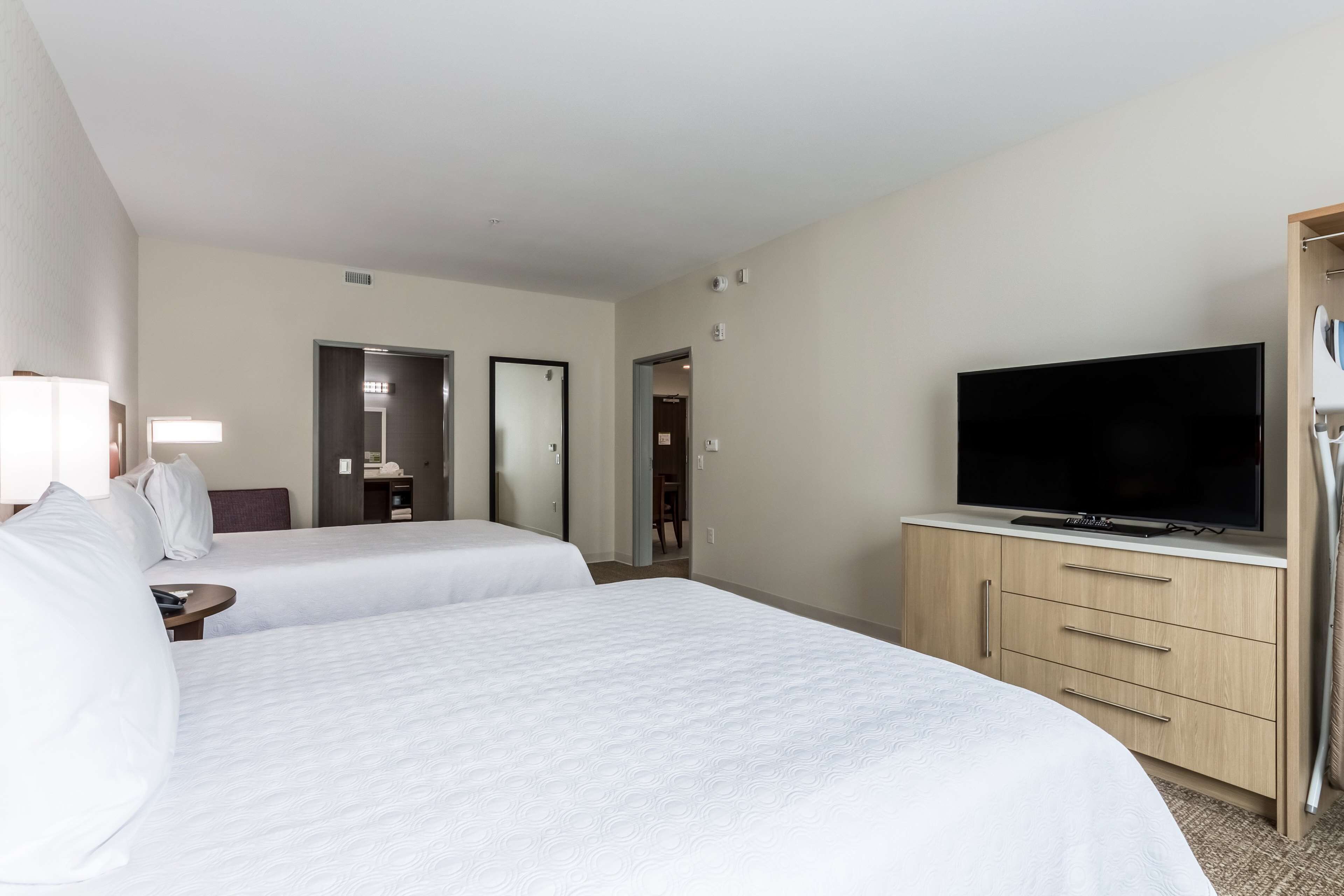 Une chambre d’hôtel avec deux lits, un téléviseur posé sur une commode en bois et un miroir au mur.