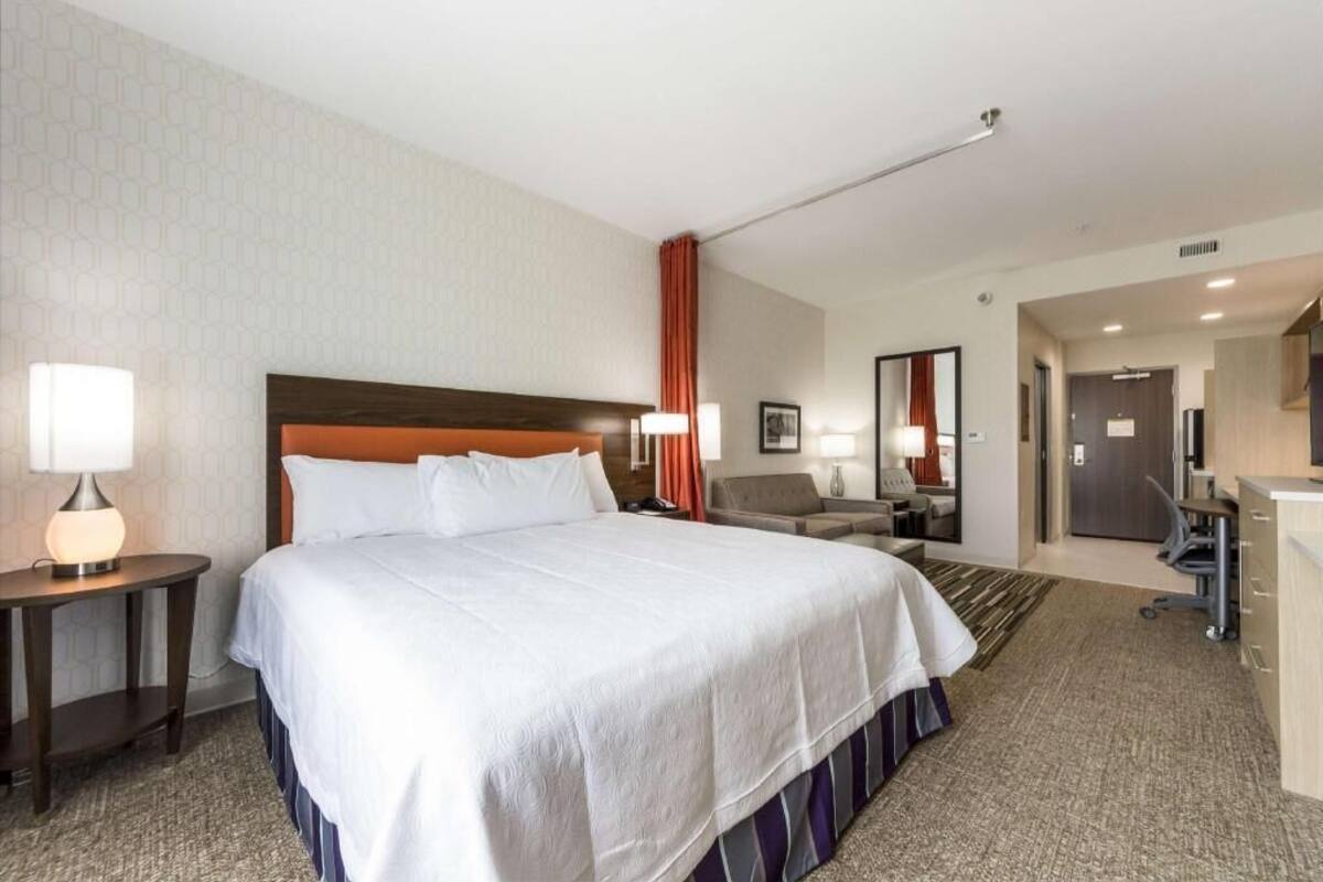 Una habitación de hotel con una cama grande, un escritorio, una silla, una lámpara y un espejo.