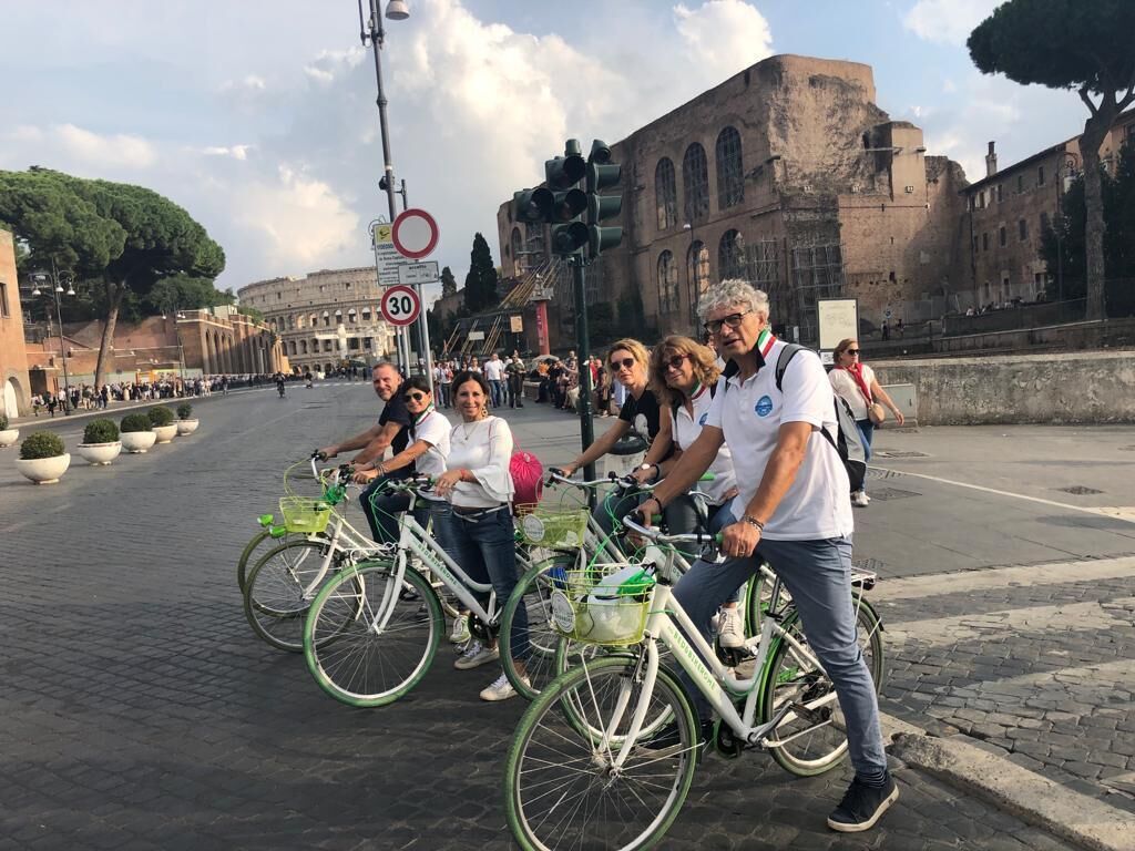 Un grupo de personas en bicicleta en una plaza histórica de la ciudad, con arquitectura antigua de fondo.