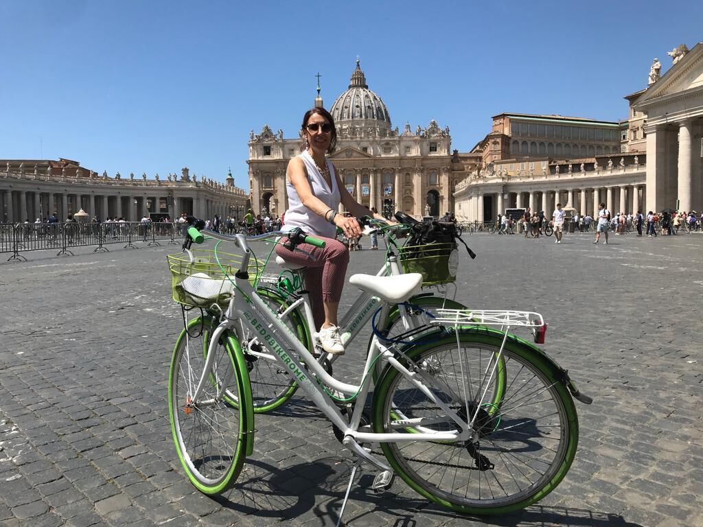 A person riding a green and white bicycle in a historic plaza with classical architecture in the background.