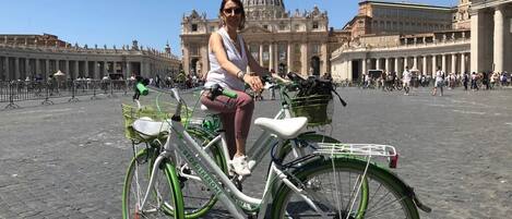 A person riding a green and white bicycle in a historic plaza with classical architecture in the background.