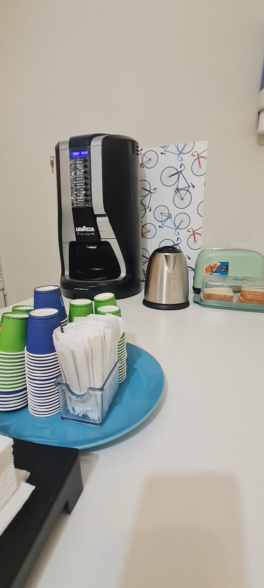 A coffee machine, stacked cups, a kettle, and a tray with napkins on a table.