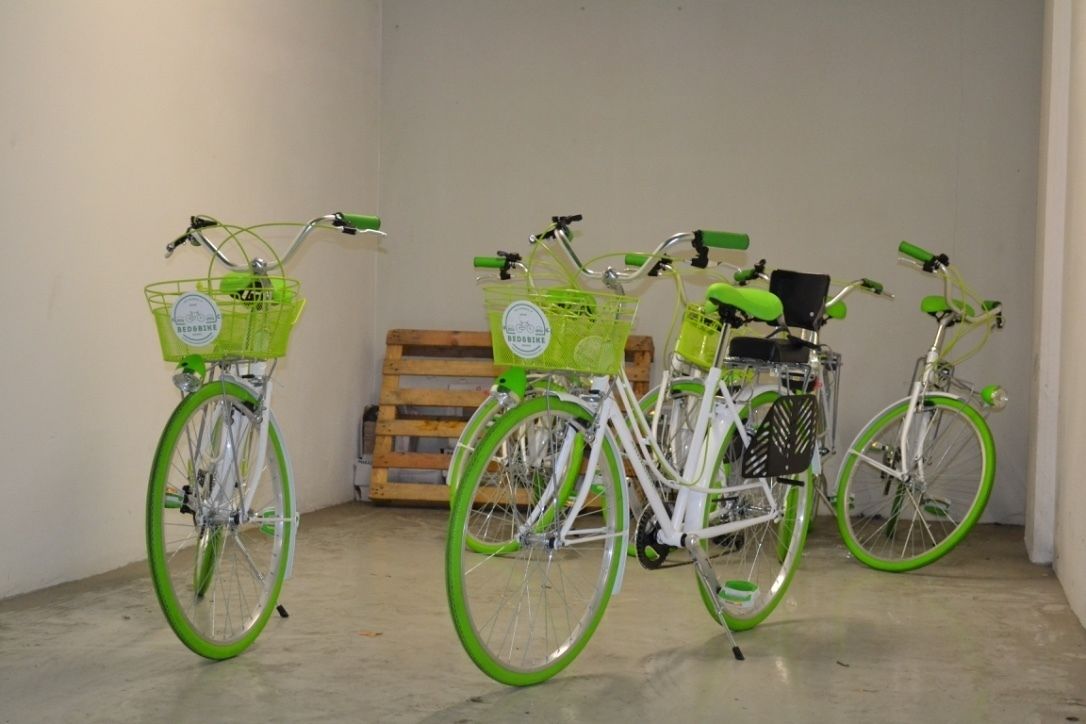 Three bicycles with green rims and baskets, parked indoors against a wall.