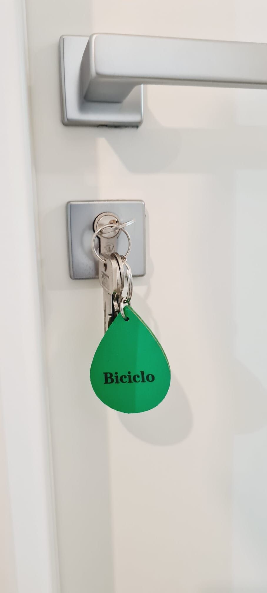 A keychain with a green tag labeled "Biciclo" attached to a door handle.