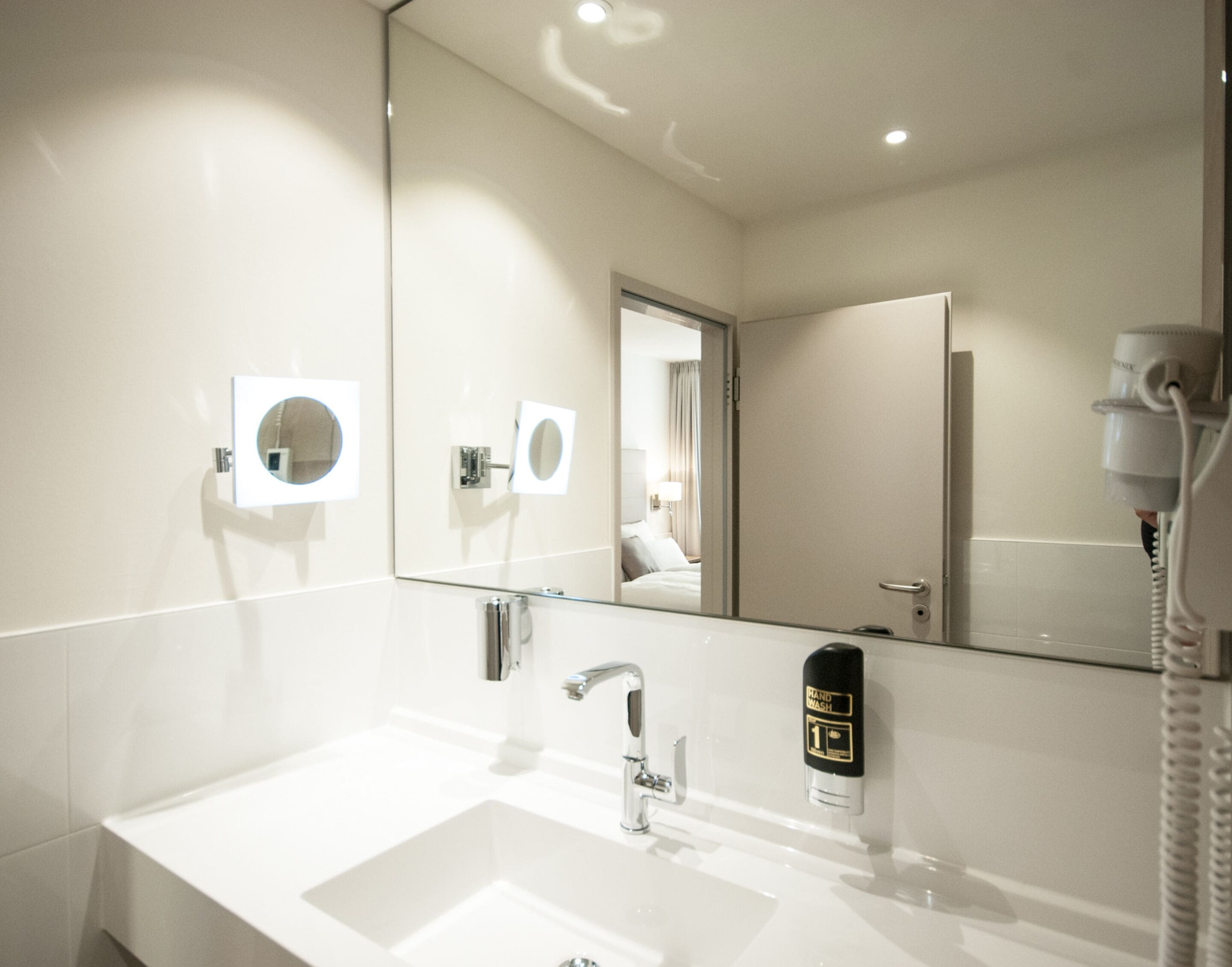 Een moderne badkamer met een wit wastafelmeubel, een spiegel en een handdesinfecteerder.