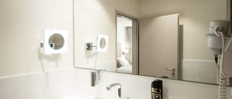 A modern bathroom with a white sink, a mirror, and a hand sanitizer dispenser.