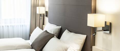 A hotel room with a large bed, two bedside lamps, and a window with curtains.