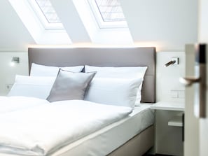 Ett modernt hotellrum med en stor säng, en sänggavel och takfönster.