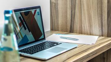 Een laptop op een houten bureau met een pen en wat documenten.